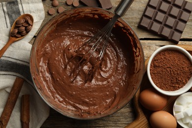 Photo of Chocolate dough in bowl among ingredients on wooden table, flat lay