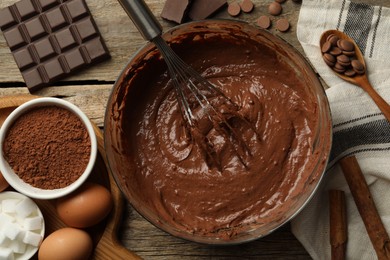 Photo of Chocolate dough in bowl among ingredients on wooden table, flat lay