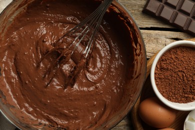 Photo of Chocolate dough in bowl among ingredients on wooden table, flat lay