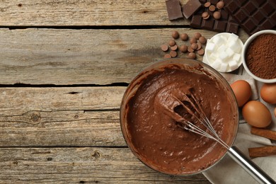 Photo of Chocolate dough in bowl and ingredients on wooden table, flat lay. Space for text