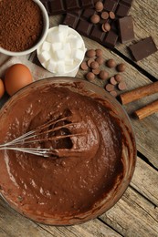 Photo of Chocolate dough in bowl and ingredients on wooden table, flat lay