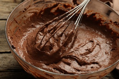 Photo of Chocolate dough in bowl and whisk on wooden table, closeup