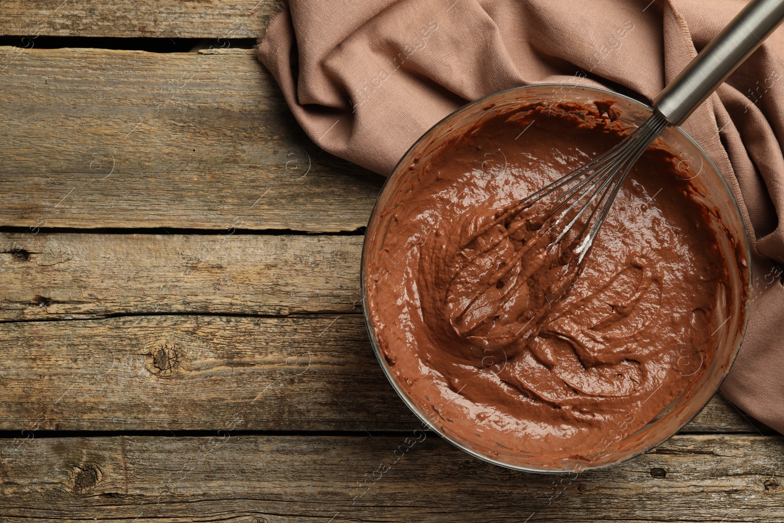 Photo of Chocolate dough in bowl and whisk on wooden table, top view. Space for text