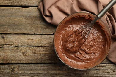 Photo of Chocolate dough in bowl and whisk on wooden table, top view. Space for text