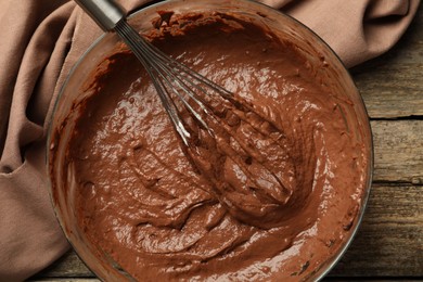 Photo of Chocolate dough in bowl and whisk on wooden table, top view