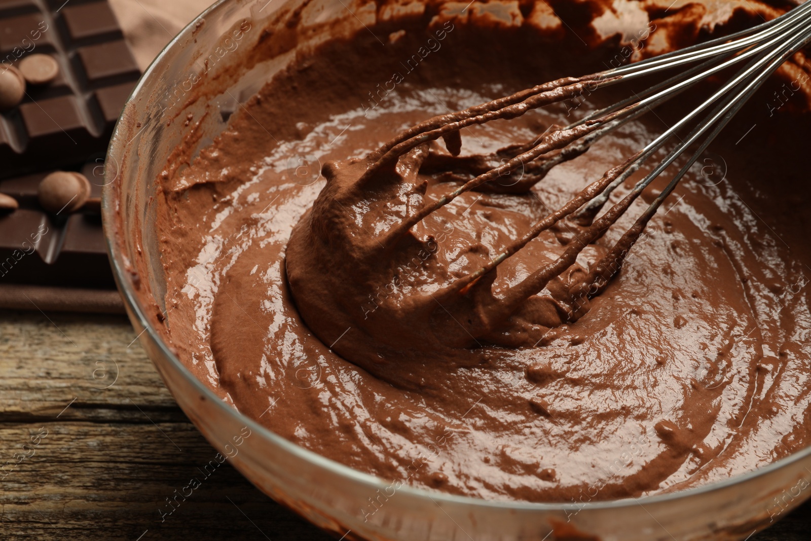 Photo of Chocolate dough in bowl and whisk on wooden table, closeup