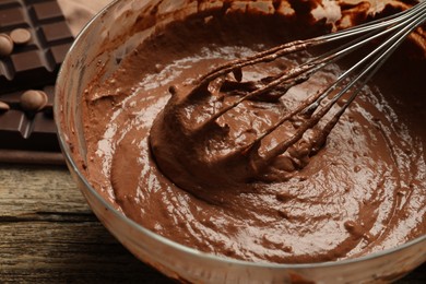 Photo of Chocolate dough in bowl and whisk on wooden table, closeup