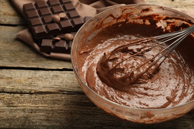 Photo of Chocolate dough in bowl and whisk on wooden table, closeup