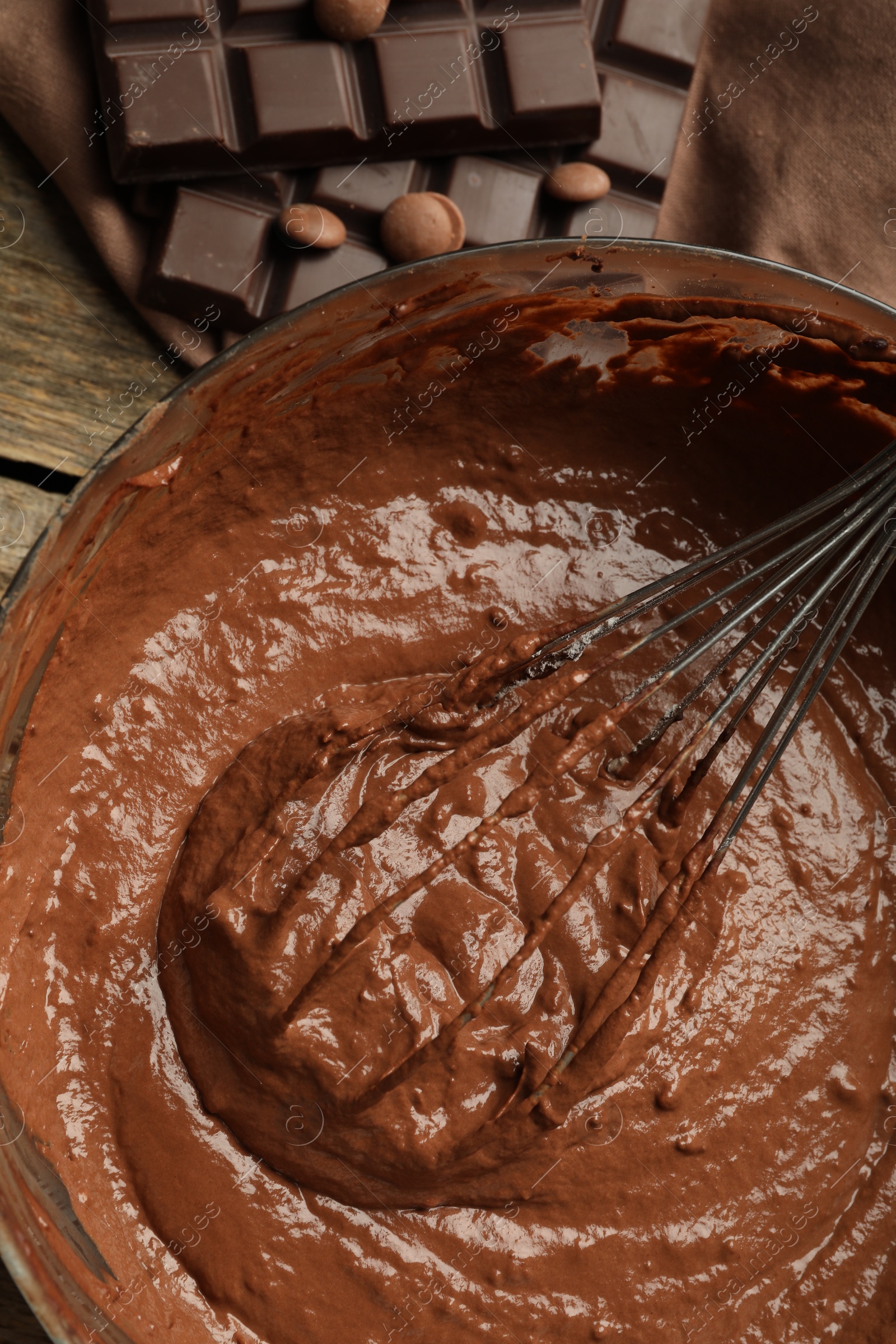 Photo of Chocolate dough in bowl and whisk on wooden table, top view