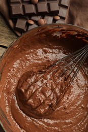 Photo of Chocolate dough in bowl and whisk on wooden table, top view