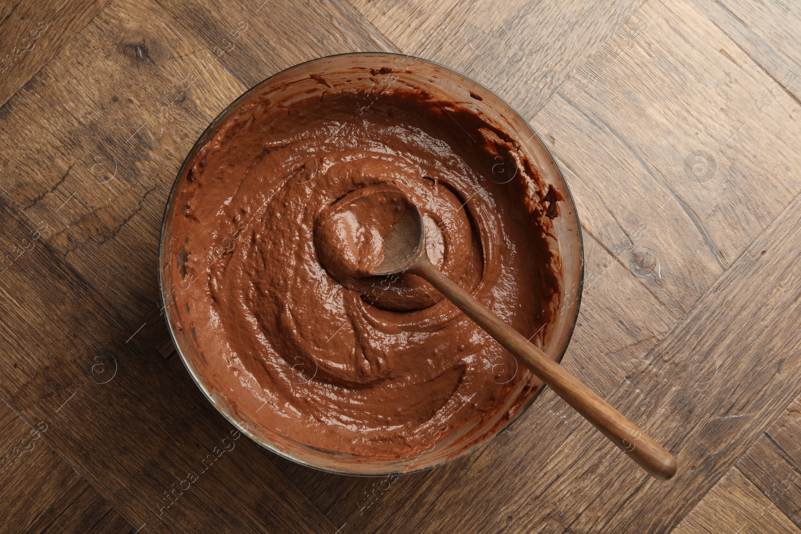 Photo of Chocolate dough in bowl and spoon on wooden table, top view