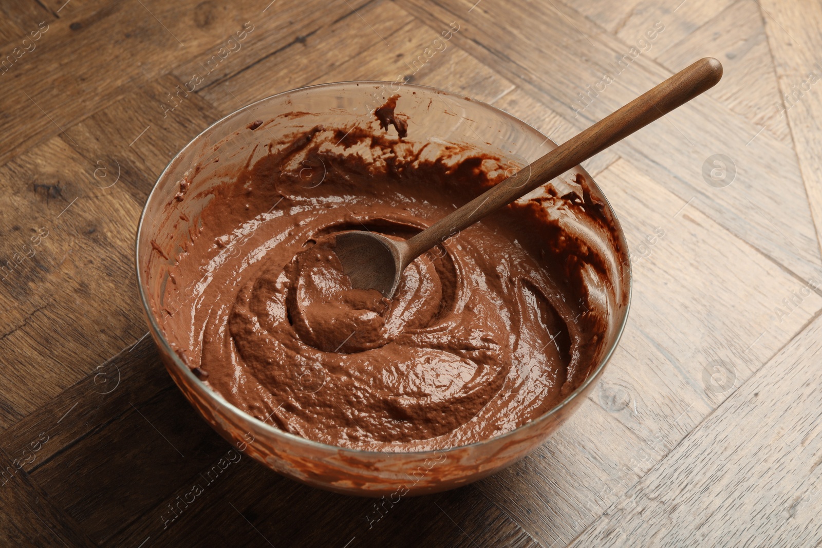 Photo of Chocolate dough in bowl and spoon on wooden table, closeup