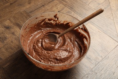 Photo of Chocolate dough in bowl and spoon on wooden table, closeup