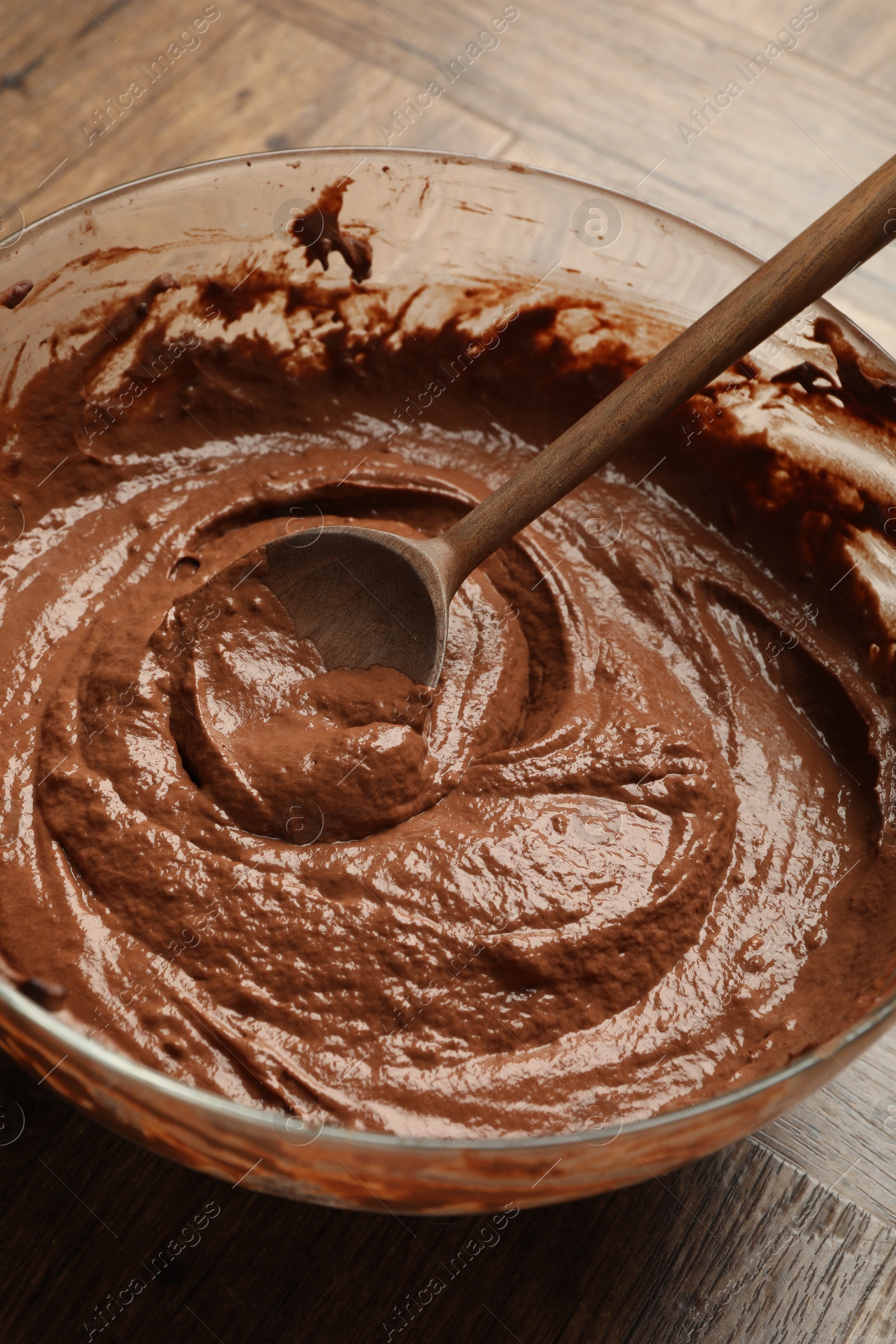 Photo of Chocolate dough in bowl and spoon on wooden table, closeup