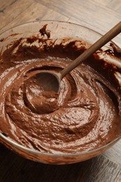 Photo of Chocolate dough in bowl and spoon on wooden table, closeup