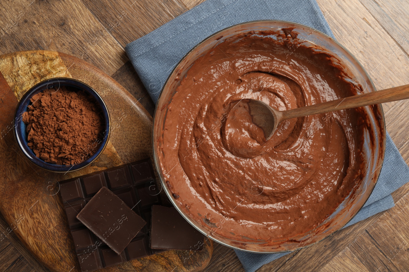 Photo of Chocolate dough in bowl, spoon and ingredients on wooden table, flat lay