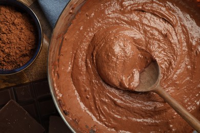 Photo of Chocolate dough in bowl, spoon and cocoa on wooden table, flat lay