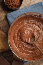 Photo of Chocolate dough in bowl, spoon and cocoa on wooden table, flat lay