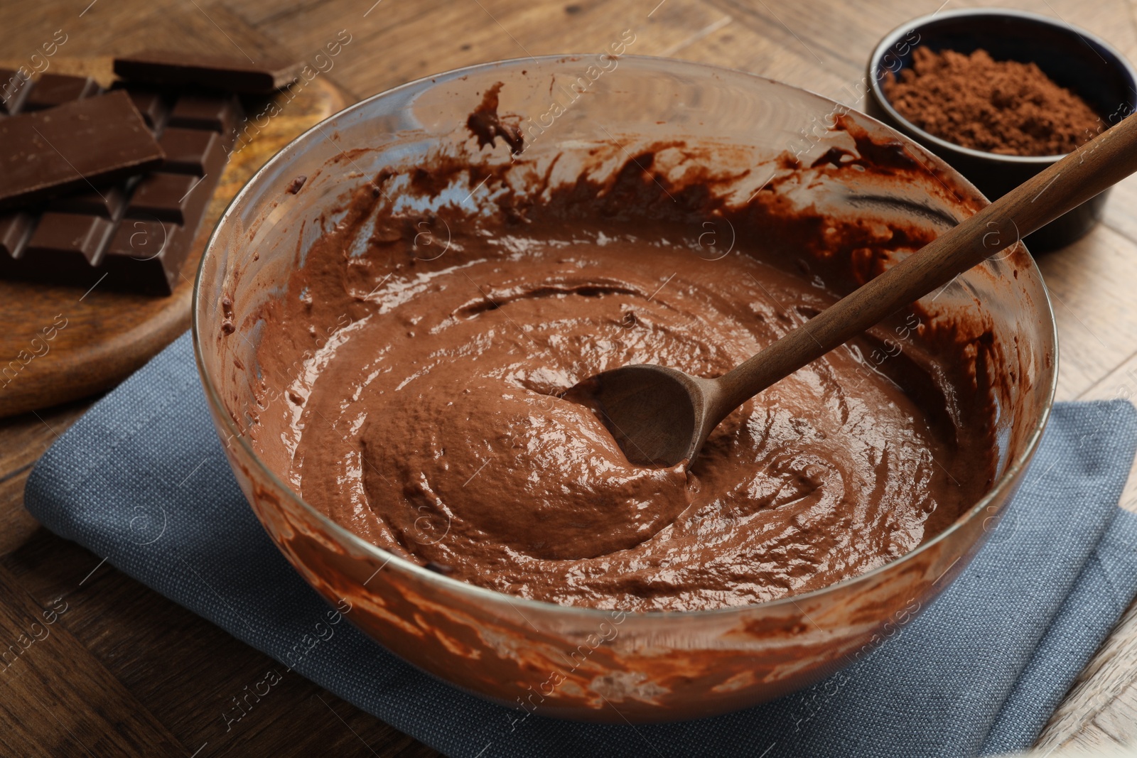 Photo of Chocolate dough and spoon in bowl on wooden table, closeup