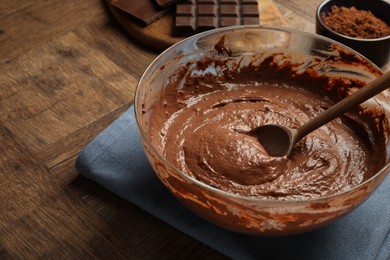 Photo of Chocolate dough and spoon in bowl on wooden table, closeup