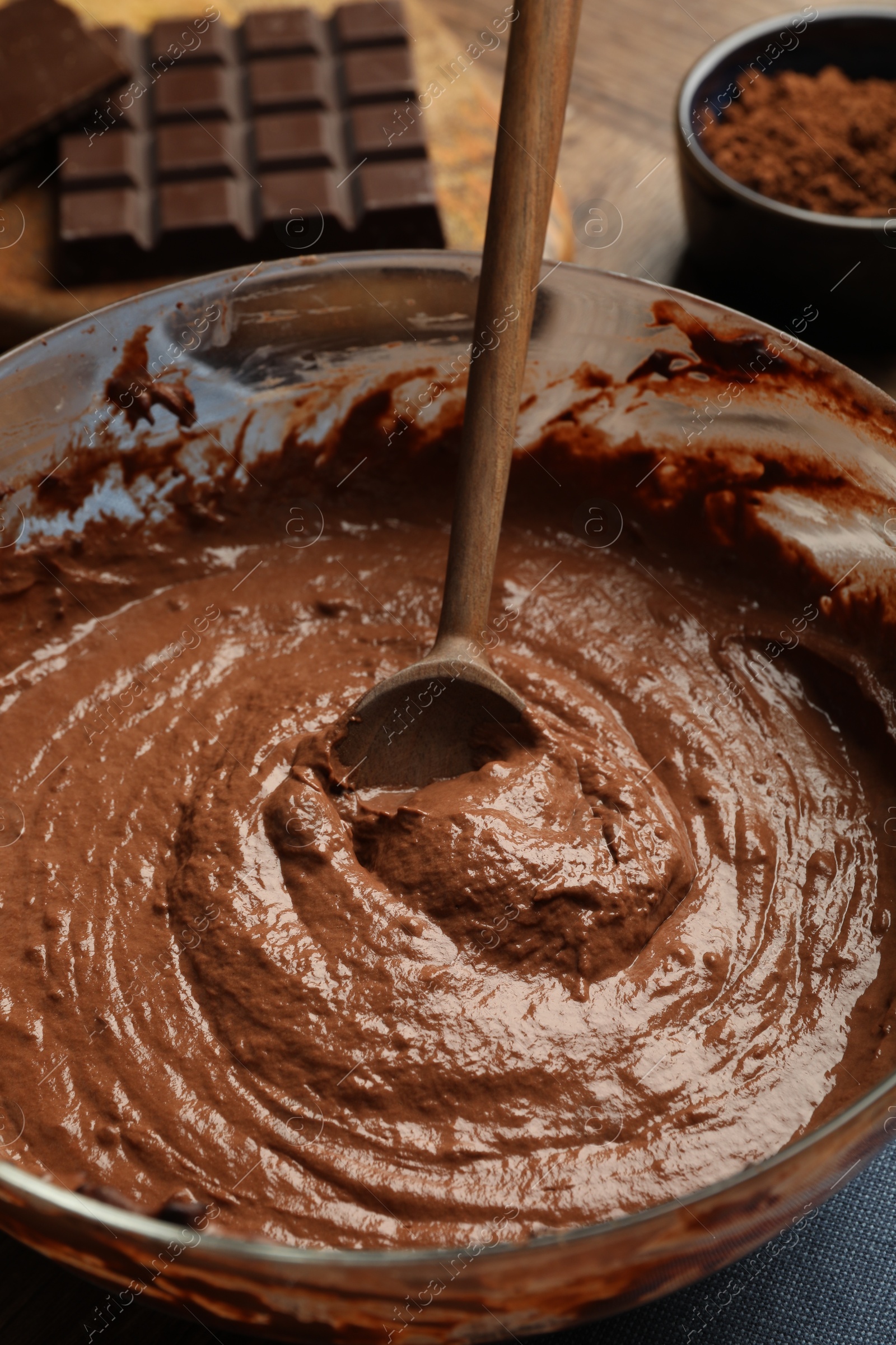 Photo of Chocolate dough and spoon in bowl on table, closeup