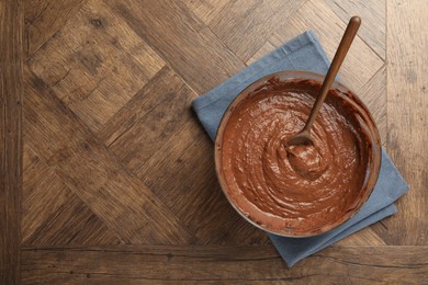 Photo of Chocolate dough in bowl and spoon on wooden table, top view. Space for text