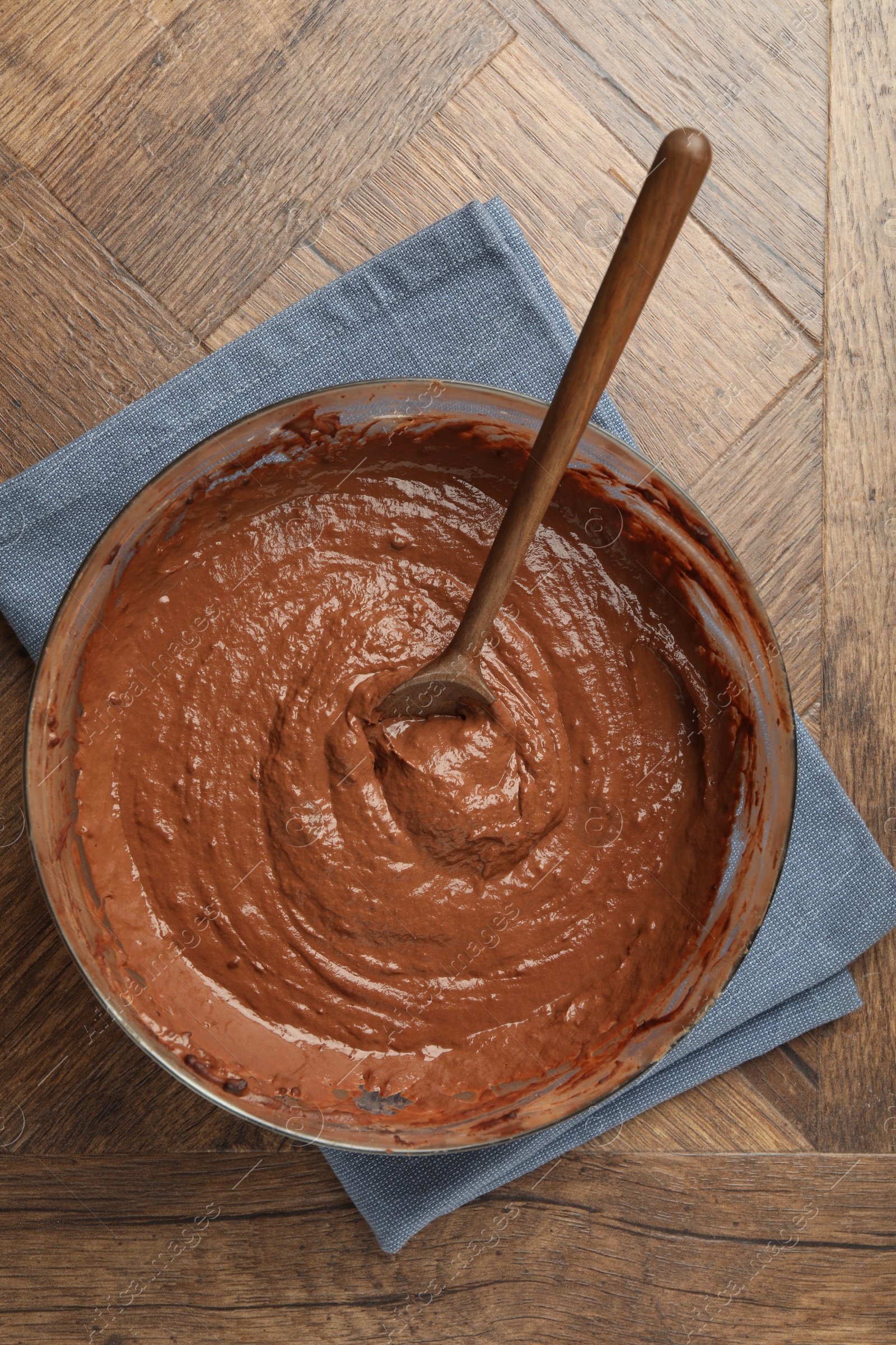 Photo of Chocolate dough in bowl and spoon on wooden table, top view