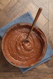 Photo of Chocolate dough in bowl and spoon on wooden table, top view