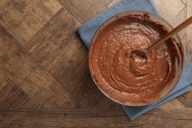 Photo of Chocolate dough in bowl and spoon on wooden table, top view. Space for text