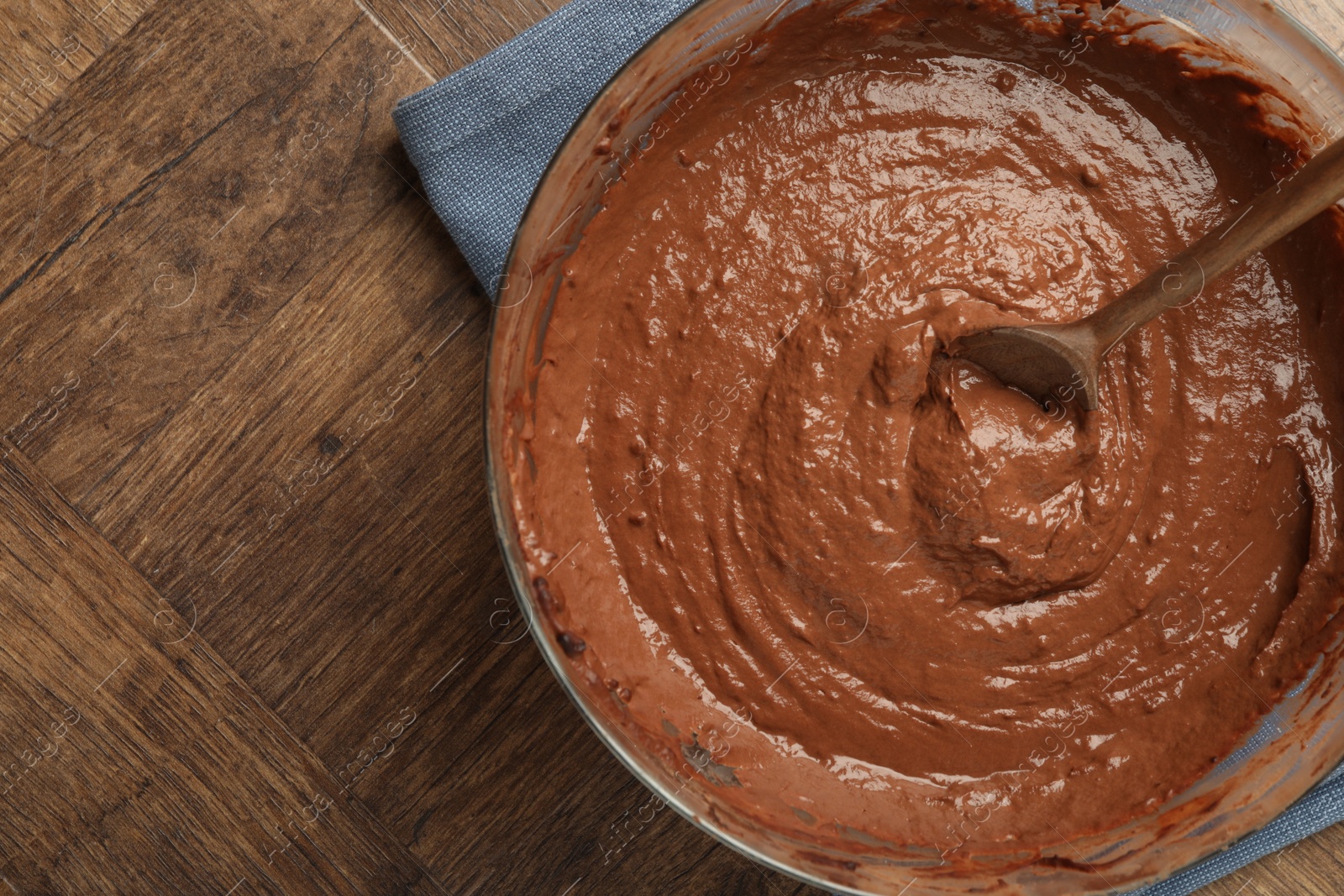 Photo of Chocolate dough in bowl and spoon on wooden table, top view. Space for text