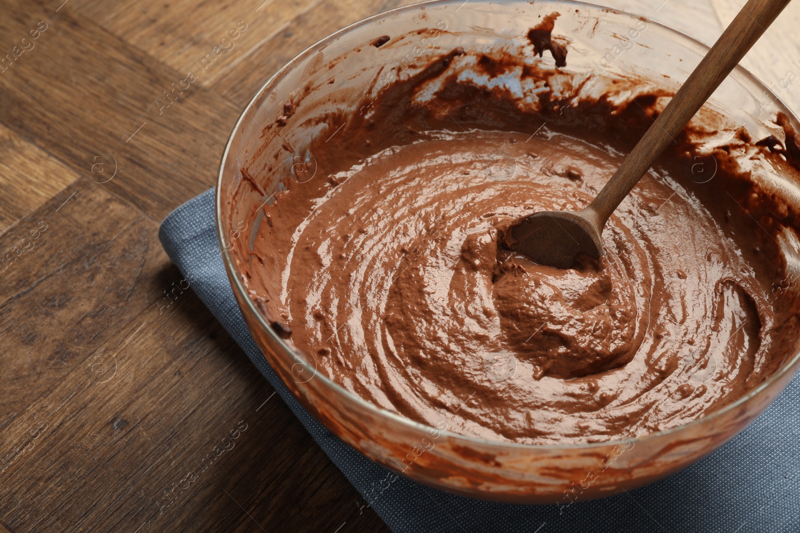 Photo of Chocolate dough in bowl and spoon on wooden table, closeup