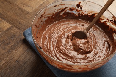 Photo of Chocolate dough in bowl and spoon on wooden table, closeup