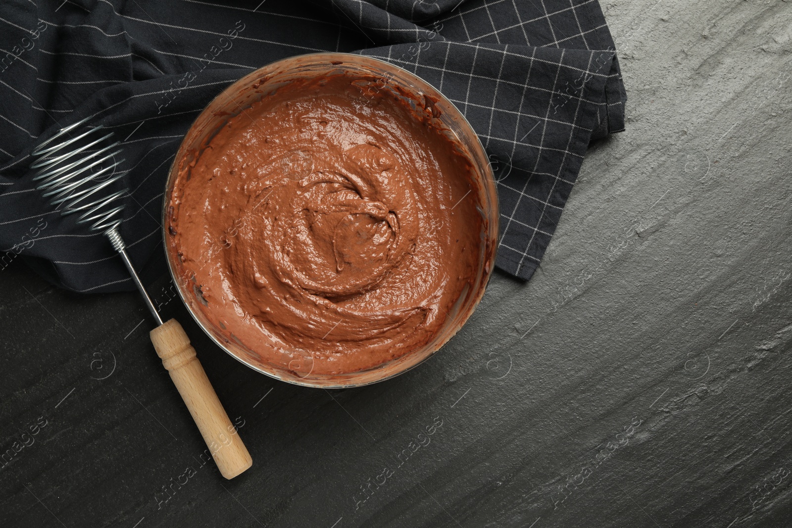 Photo of Chocolate dough in bowl and whisk on dark textured table, flat lay. Space for text