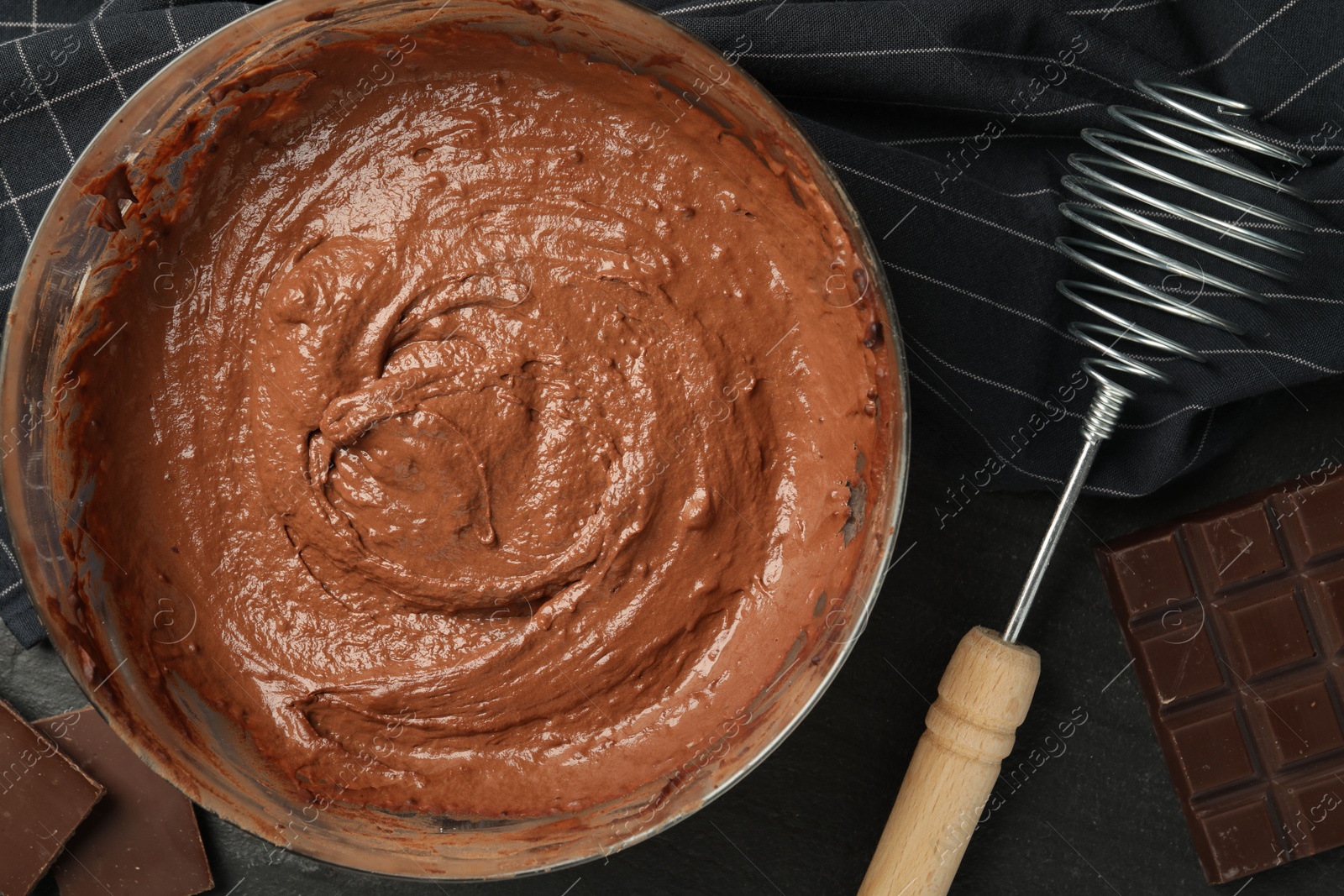 Photo of Chocolate dough in bowl and whisk on dark table, flat lay