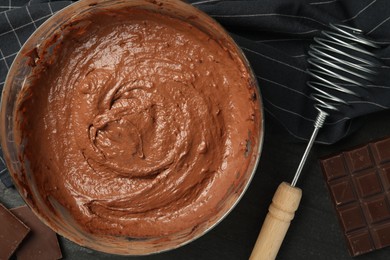 Photo of Chocolate dough in bowl and whisk on dark table, flat lay