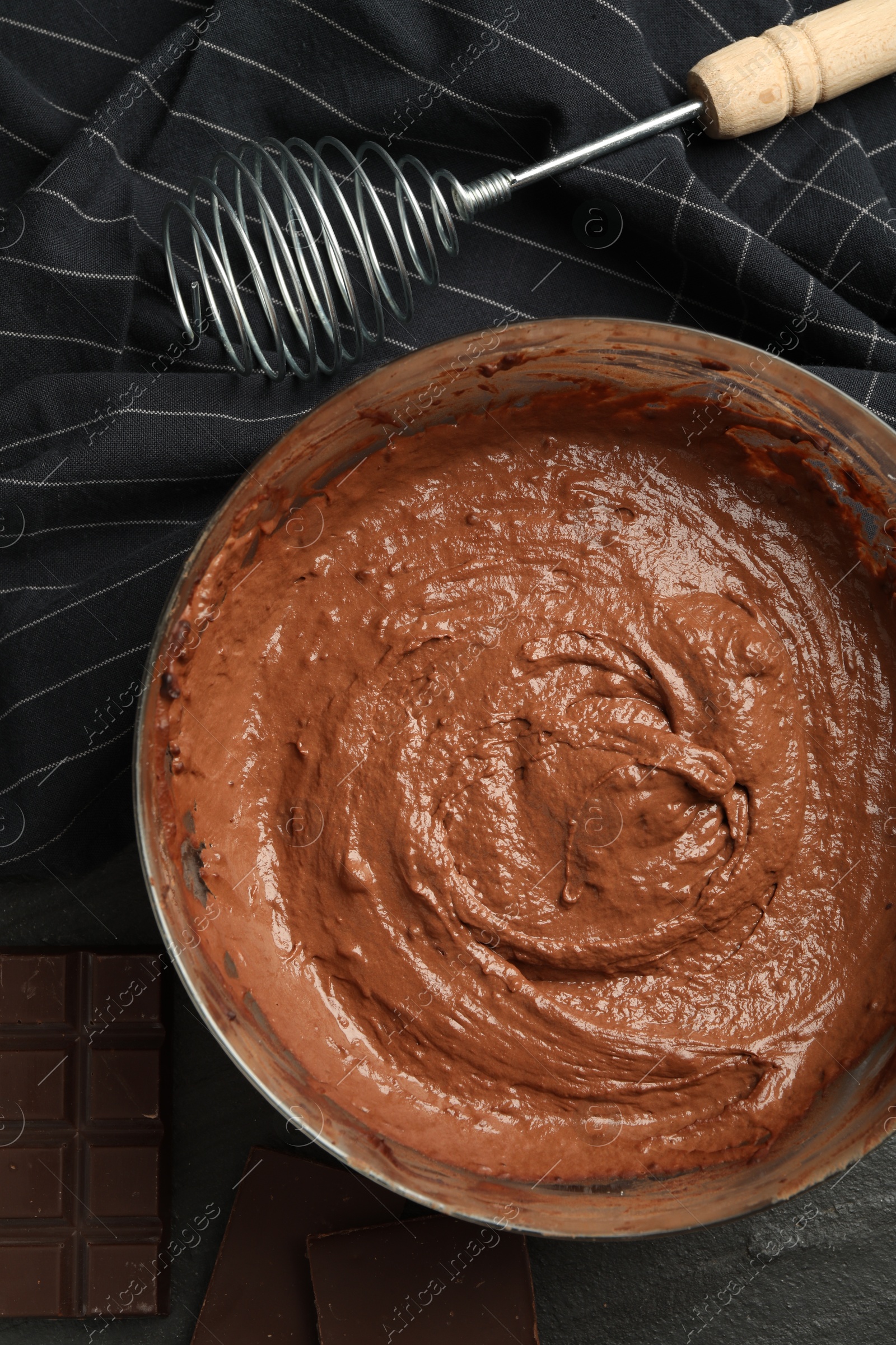 Photo of Chocolate dough in bowl and whisk on dark table, flat lay