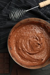 Photo of Chocolate dough in bowl and whisk on dark table, flat lay