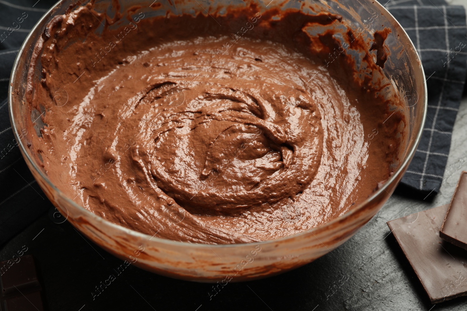 Photo of Chocolate dough in bowl and whisk on dark table, closeup