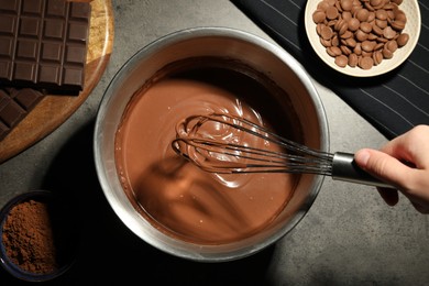 Photo of Woman mixing chocolate dough with whisk at grey table, top view