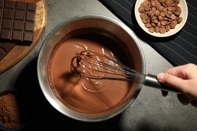 Photo of Woman mixing chocolate dough with whisk at grey table, top view