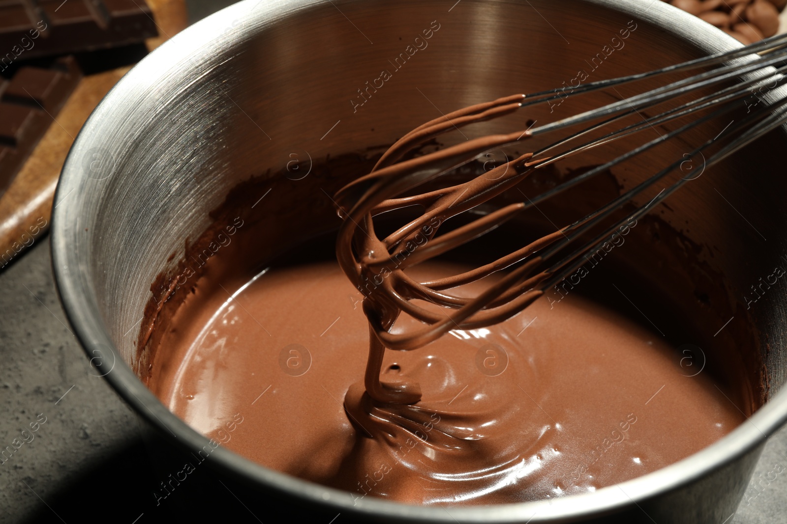 Photo of Chocolate dough dripping from whisk into bowl on table, closeup