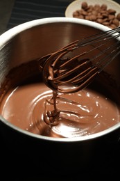 Photo of Chocolate dough dripping from whisk into bowl on table, closeup