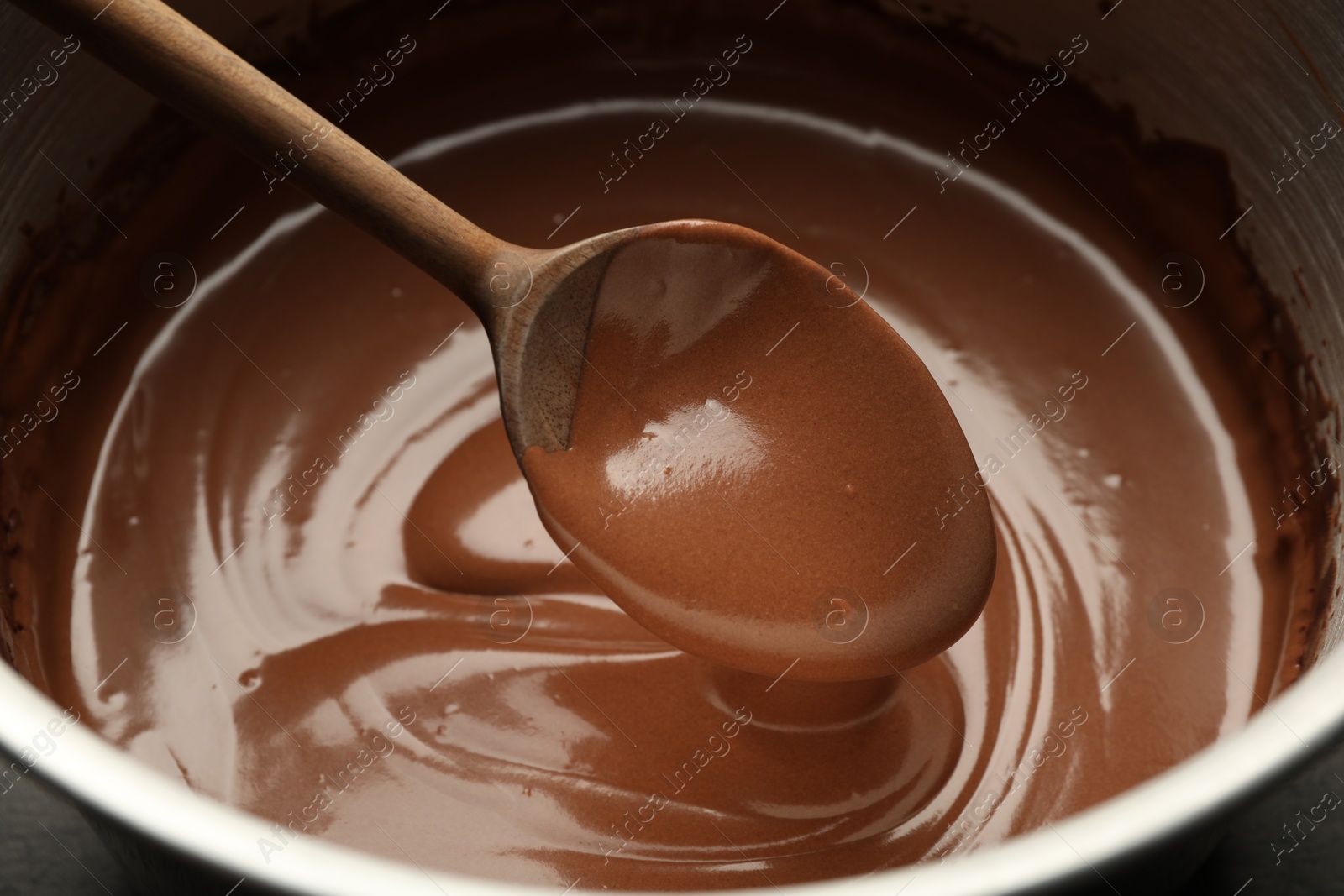 Photo of Chocolate dough dripping from spoon into bowl, closeup