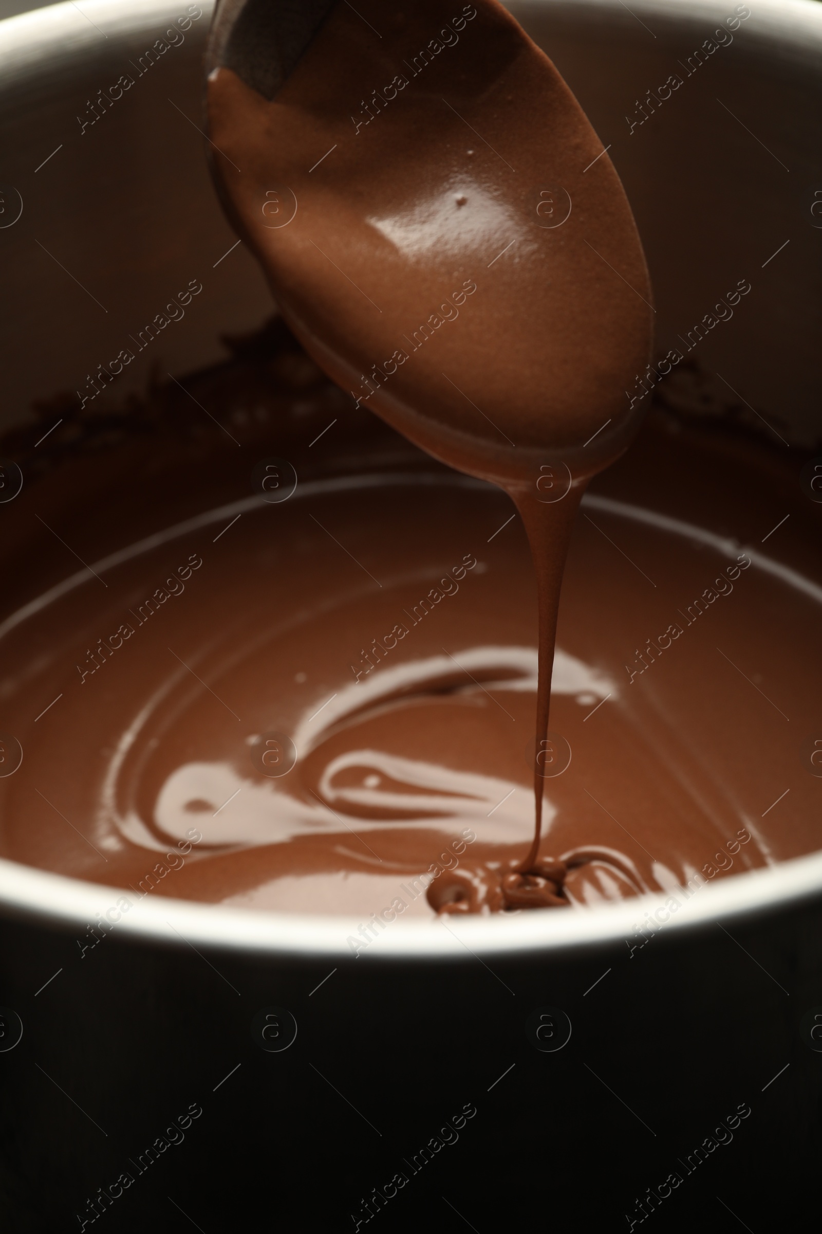 Photo of Chocolate dough dripping from spoon into bowl, closeup