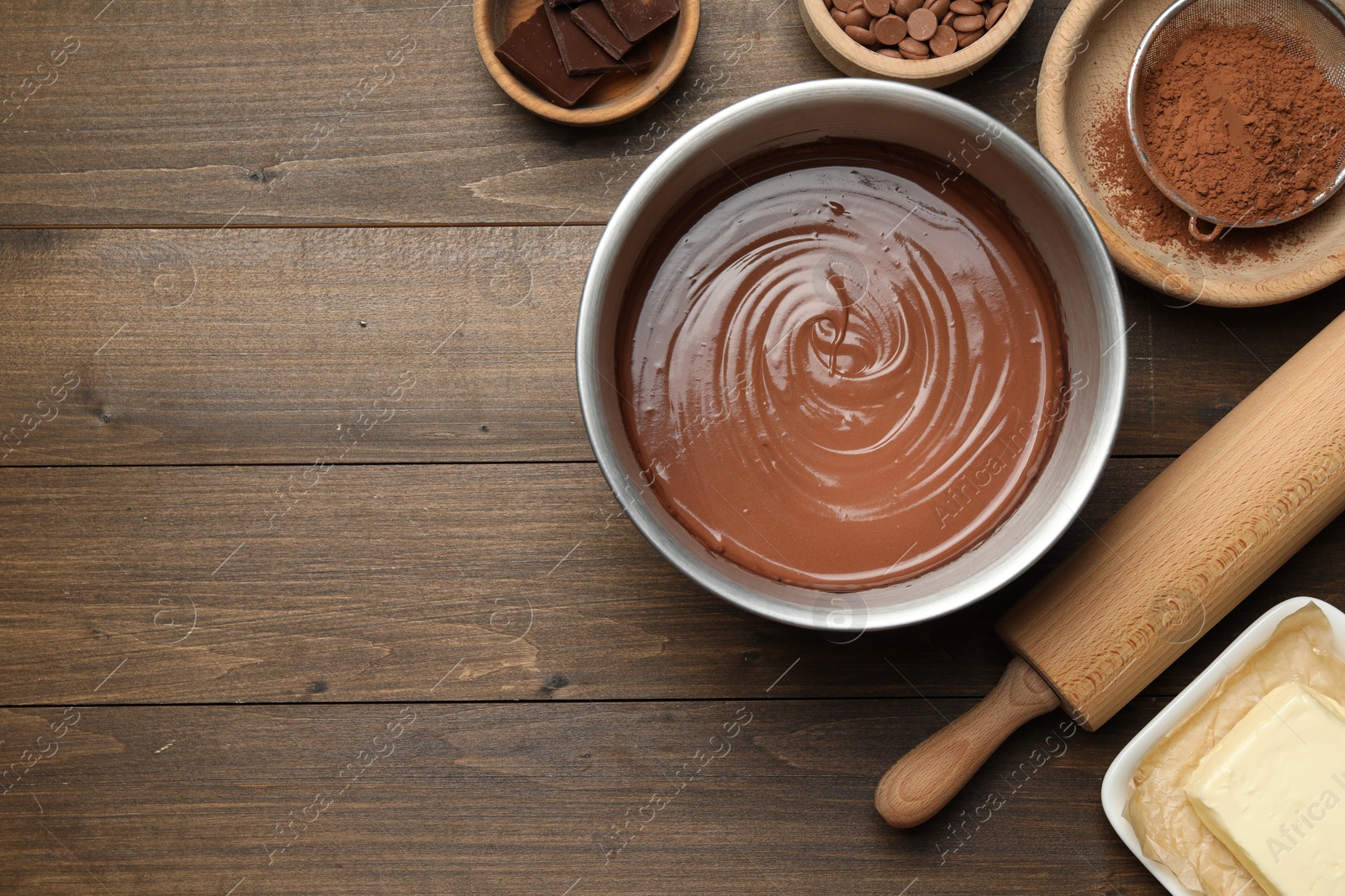 Photo of Chocolate dough in bowl and ingredients on wooden table, flat lay. Space for text