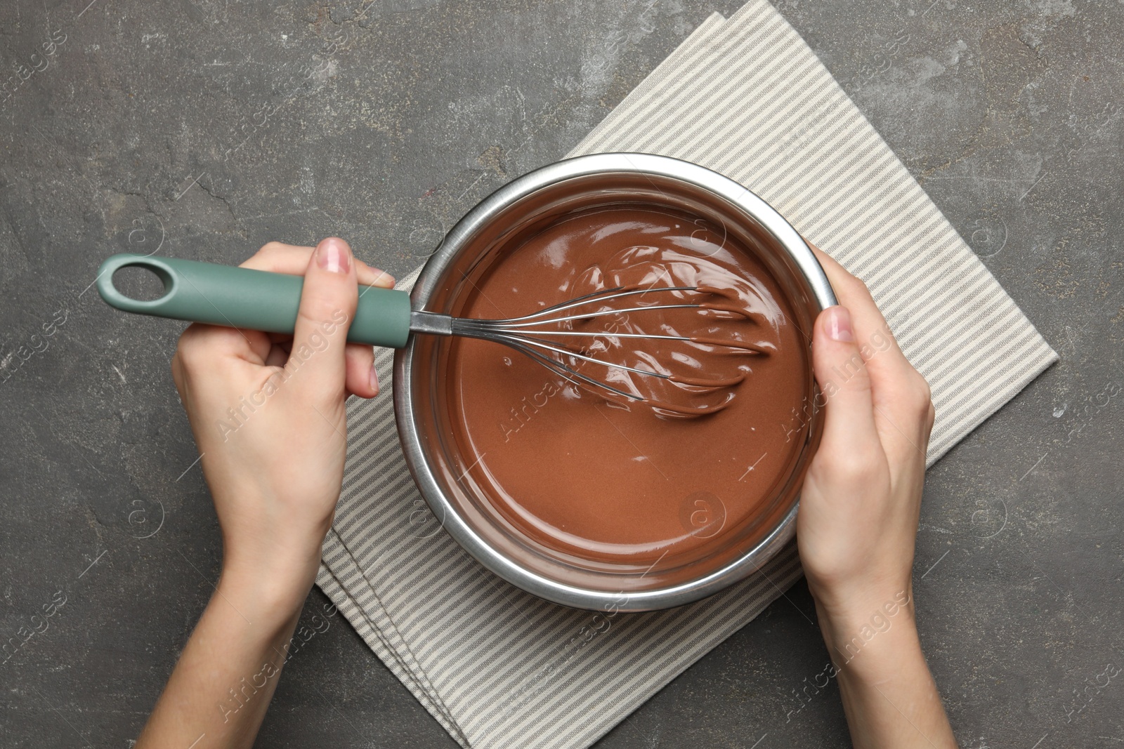 Photo of Woman mixing chocolate dough with whisk at grey table, top view