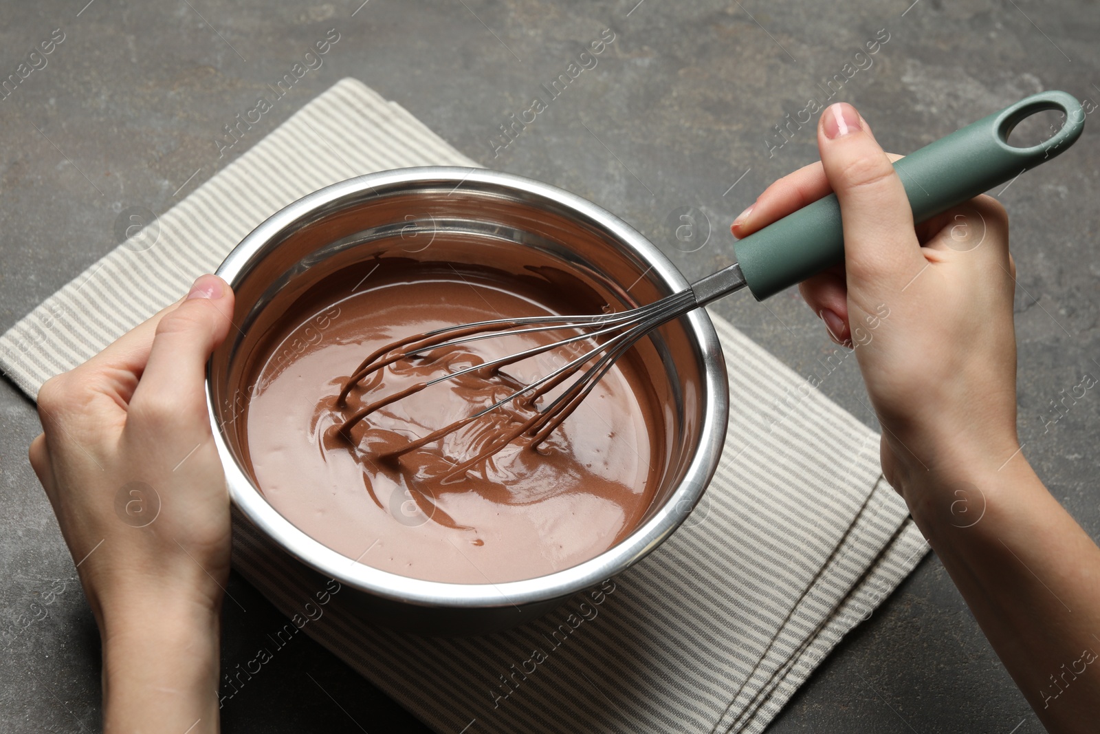 Photo of Woman mixing chocolate dough with whisk at grey table, closeup