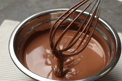 Photo of Chocolate dough dripping from whisk into bowl on table, closeup