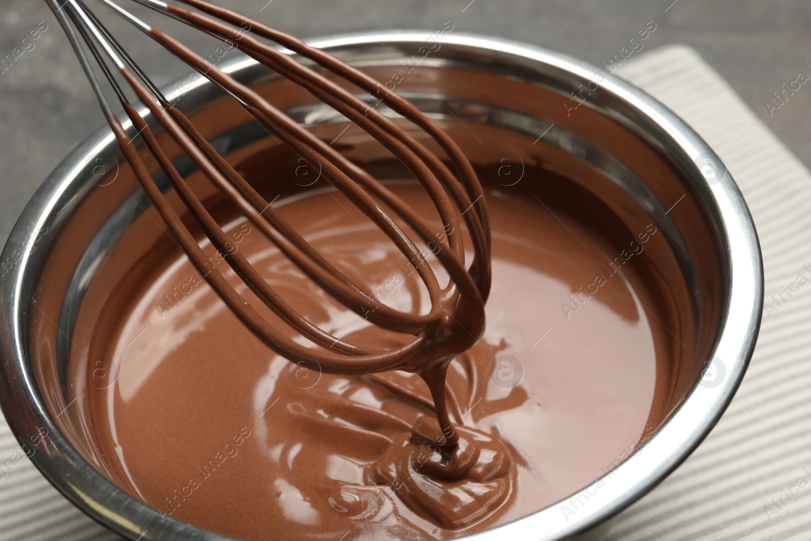 Photo of Chocolate dough dripping from whisk into bowl on table, closeup