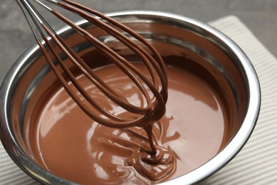 Photo of Chocolate dough dripping from whisk into bowl on table, closeup